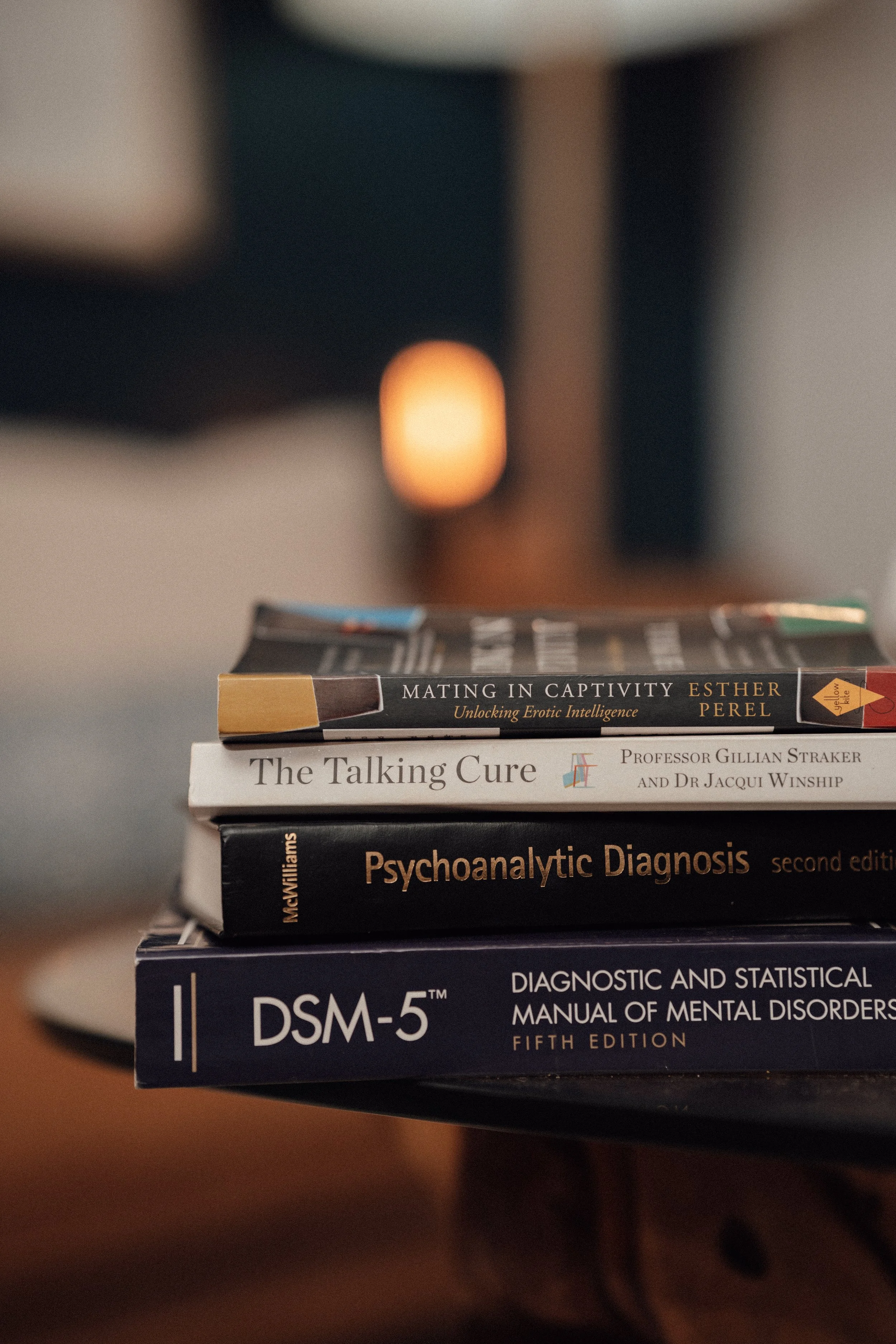 Stack of four psychology books on a wooden surface. Titles include 'Mating in Captivity,' 'The Talking Cure,' 'Psychoanalytic Diagnosis,' and 'DSM-5'.