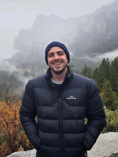 Kurt Young, performance psychologist, smiling to camera in front of misty mountains.